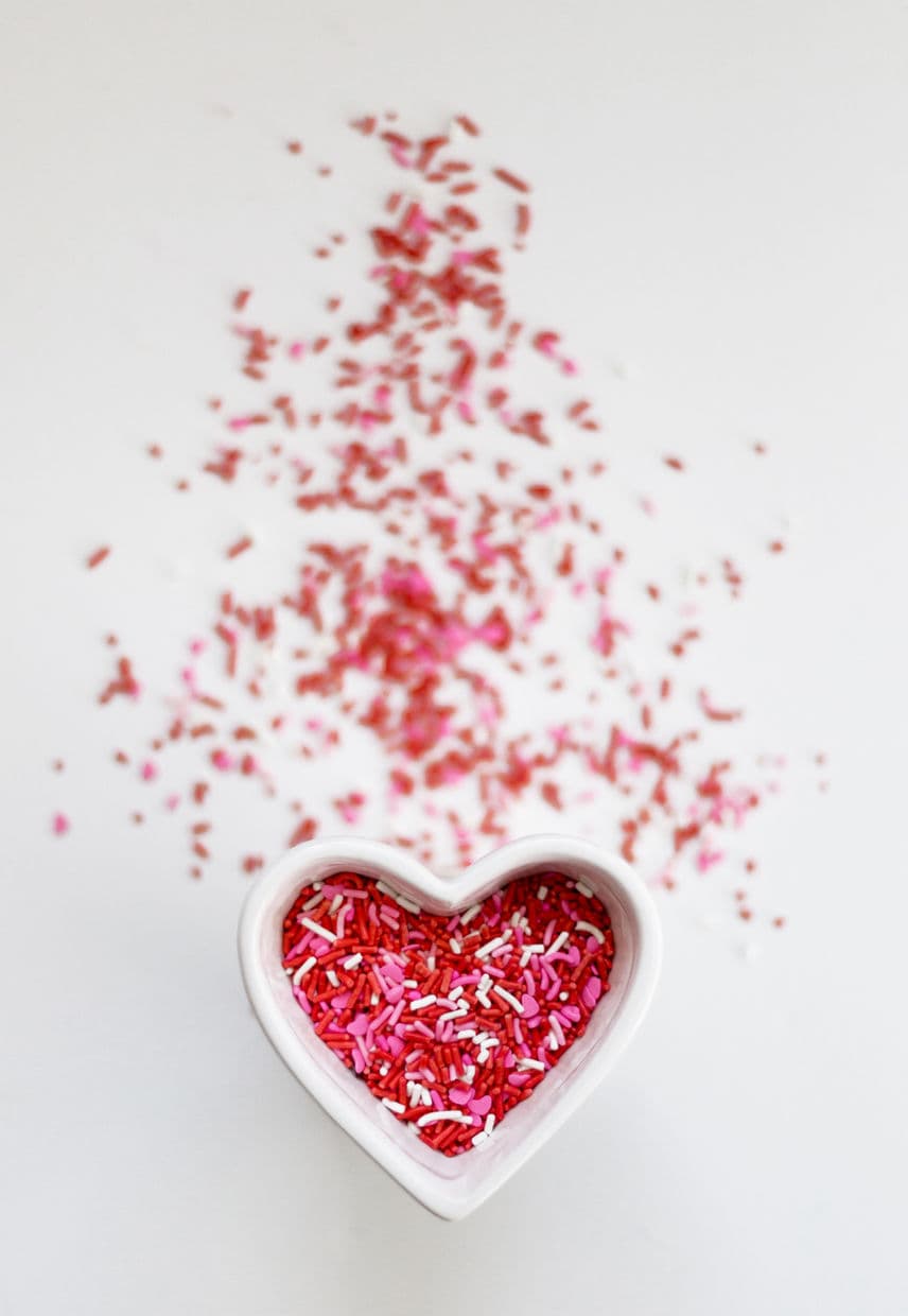 Pink sprinkles spilling from a heart-shaped dish